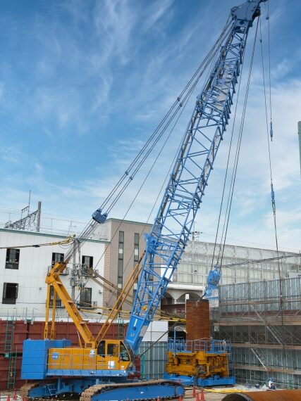 建設現場で使用されるクローラクレーン。長大なブームで資材を吊り上げ、旋回させる揚重機械